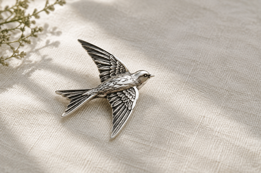 Illustrative sculptural silver bird brooch with darkened feather recesses on pale linen