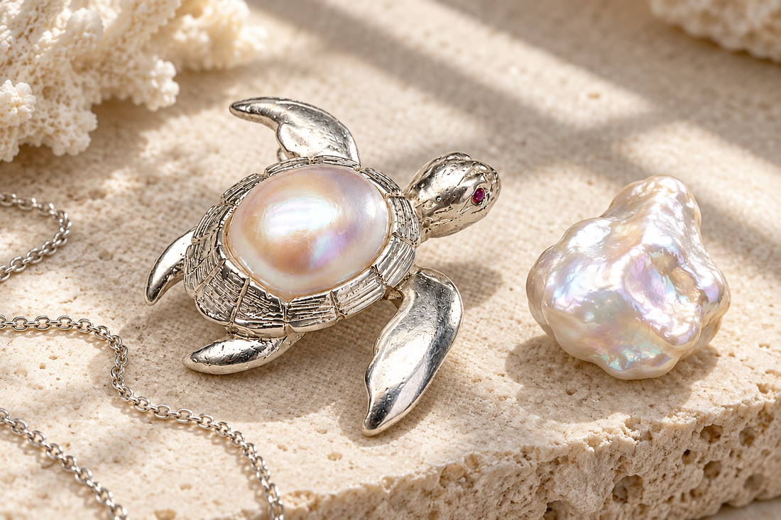 Handcrafted HEWREN sterling silver sea turtle brooch with iridescent baroque pearl carapace beside a raw natural baroque pearl on travertine stone