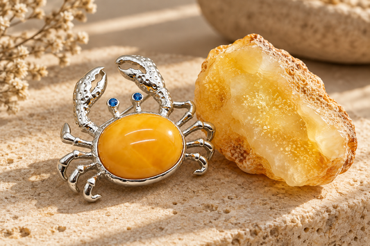 HEWREN handcrafted sterling silver crab brooch with beeswax amber cabochon beside a raw Baltic milky amber specimen on limestone