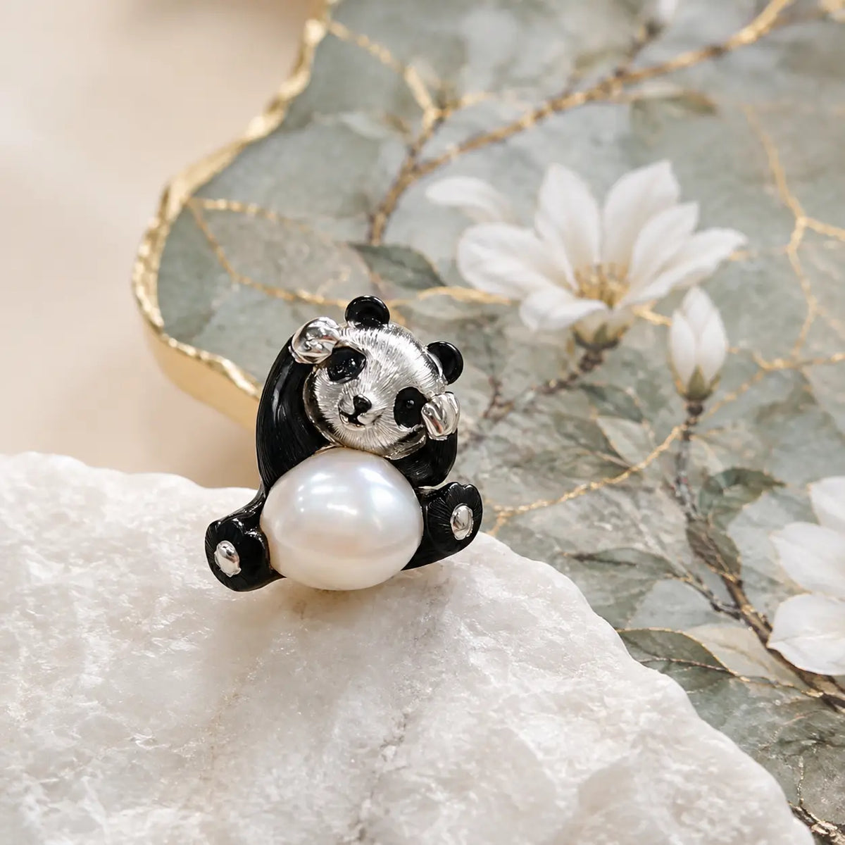 Hewren Jewelry sterling silver panda brooch pendant with black enamel details and a lustrous baroque pearl belly on white stone beside a floral dish