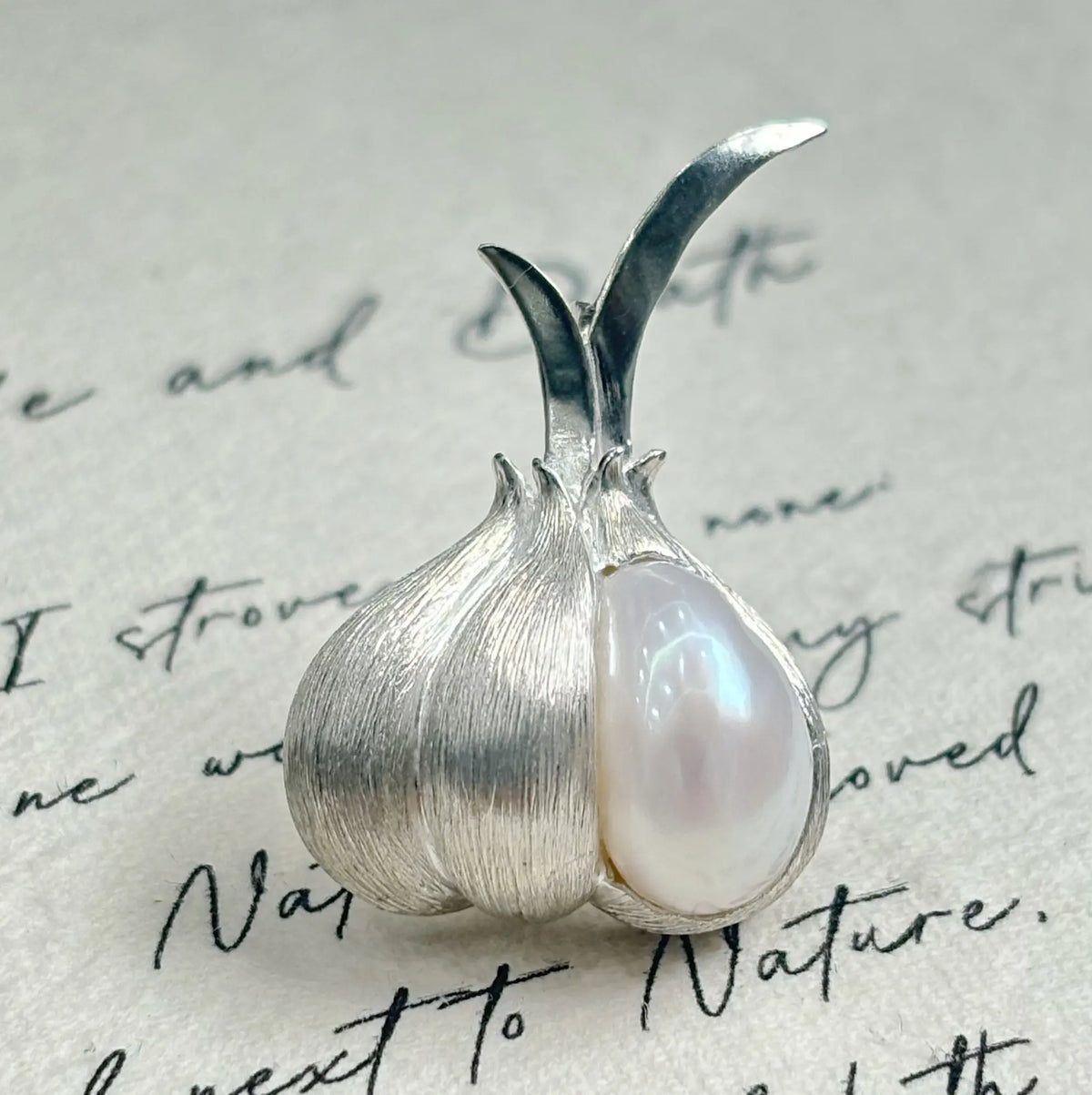 baroque pearl clove peeled garlic silver brooch detail — jewelry close-up photo