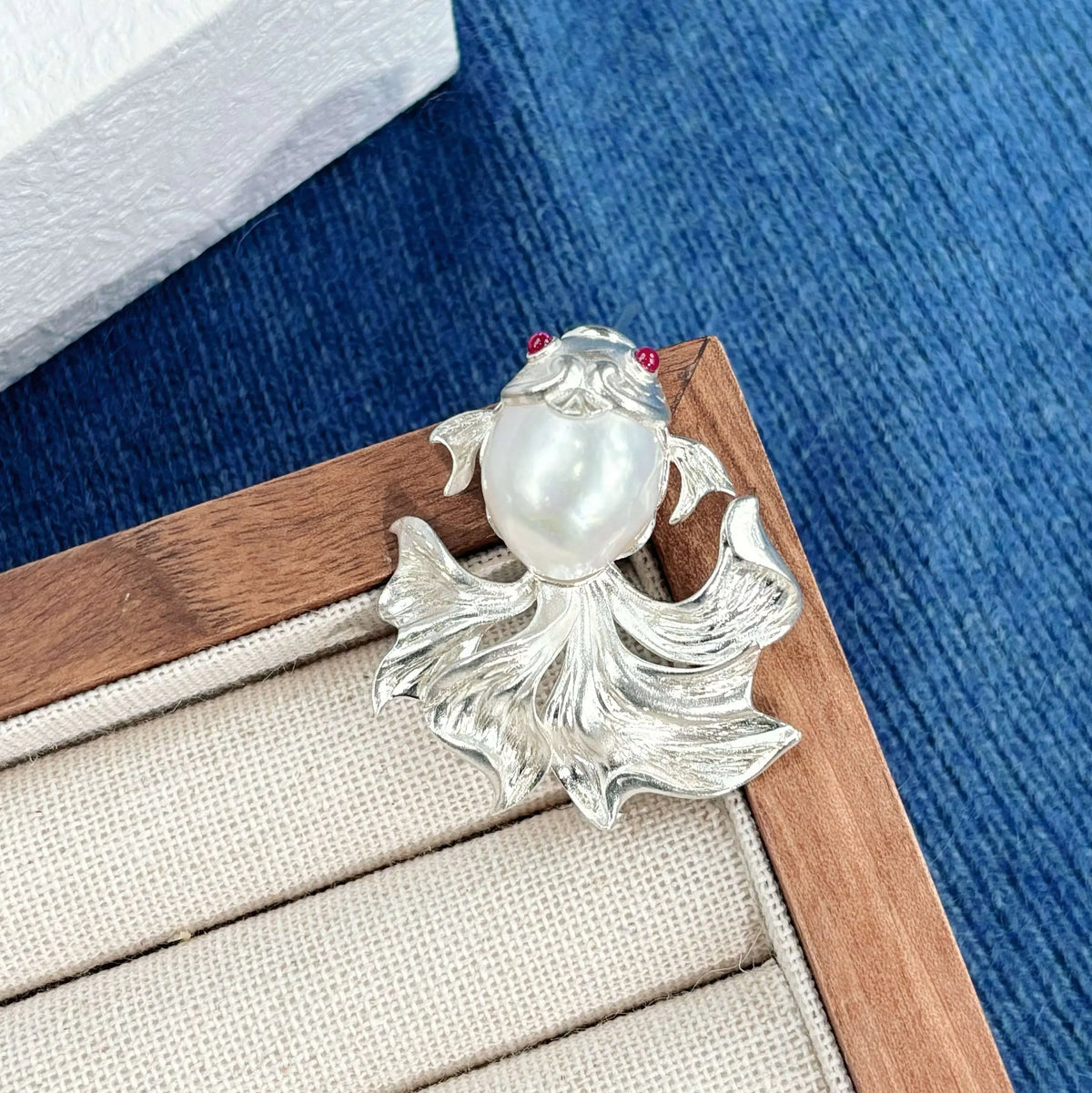 Sterling silver fan-tail goldfish brooch pinned to textile — handmade jewelry detail