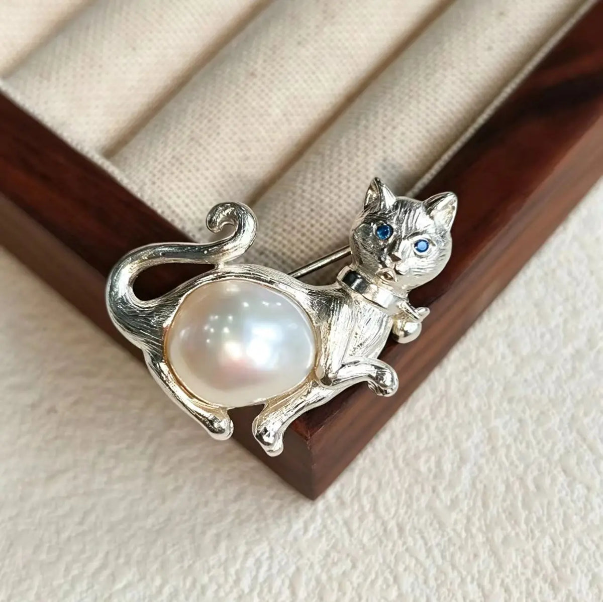 Sterling silver paw-raised cat brooch pinned to textile — handmade jewelry detail